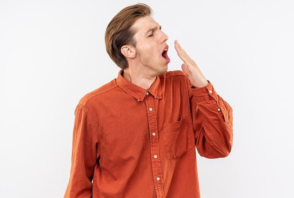 A person with underbite in a brown shirt yawns, momentarily indulging in mouth breathing, against a plain white background in San Antonio, TX