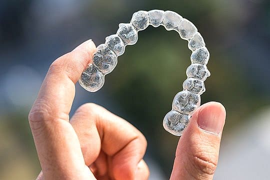 A hand gently holds an Invisalign clear dental aligner against a softly blurred background in San Antonio, TX
