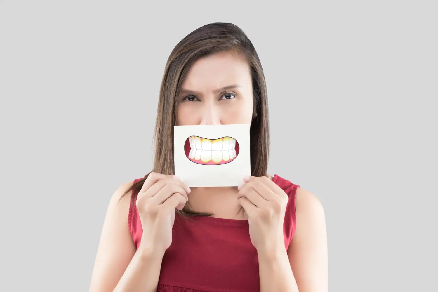 Person holding a card with an illustration of an underbite in front of their mouth, wearing a red top, against a gray background in San Antonio, TX