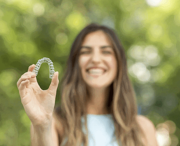 Person outdoors, smiling while holding a clear dental aligner. You might wonder, "Can Invisalign be covered by insurance?" It's worth diving into your policy to find out and make that dazzling smile even easier on the wallet in San Antonio, TX