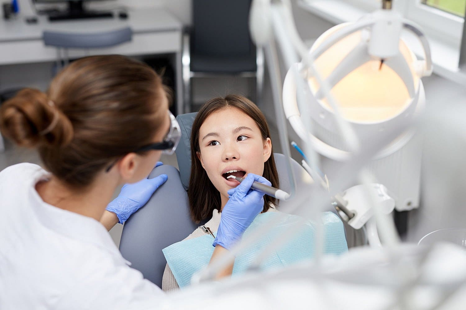 A dentist wearing gloves examines a patient's teeth using dental tools in a clinic setting in San Antonio, TX, checking for issues such as tongue thrust and other orthodontic concerns.