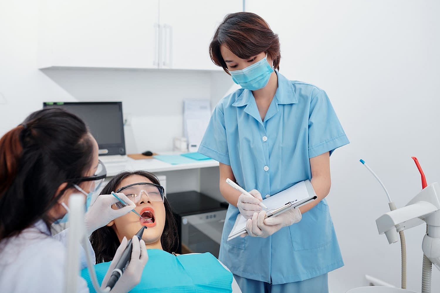 A dentist and an assistant in blue uniforms perform a procedure on a patient with metal braces, seated comfortably in a chair. Dental tools and equipment are neatly arranged in the background, ensuring precision and care in San Antonio, TX