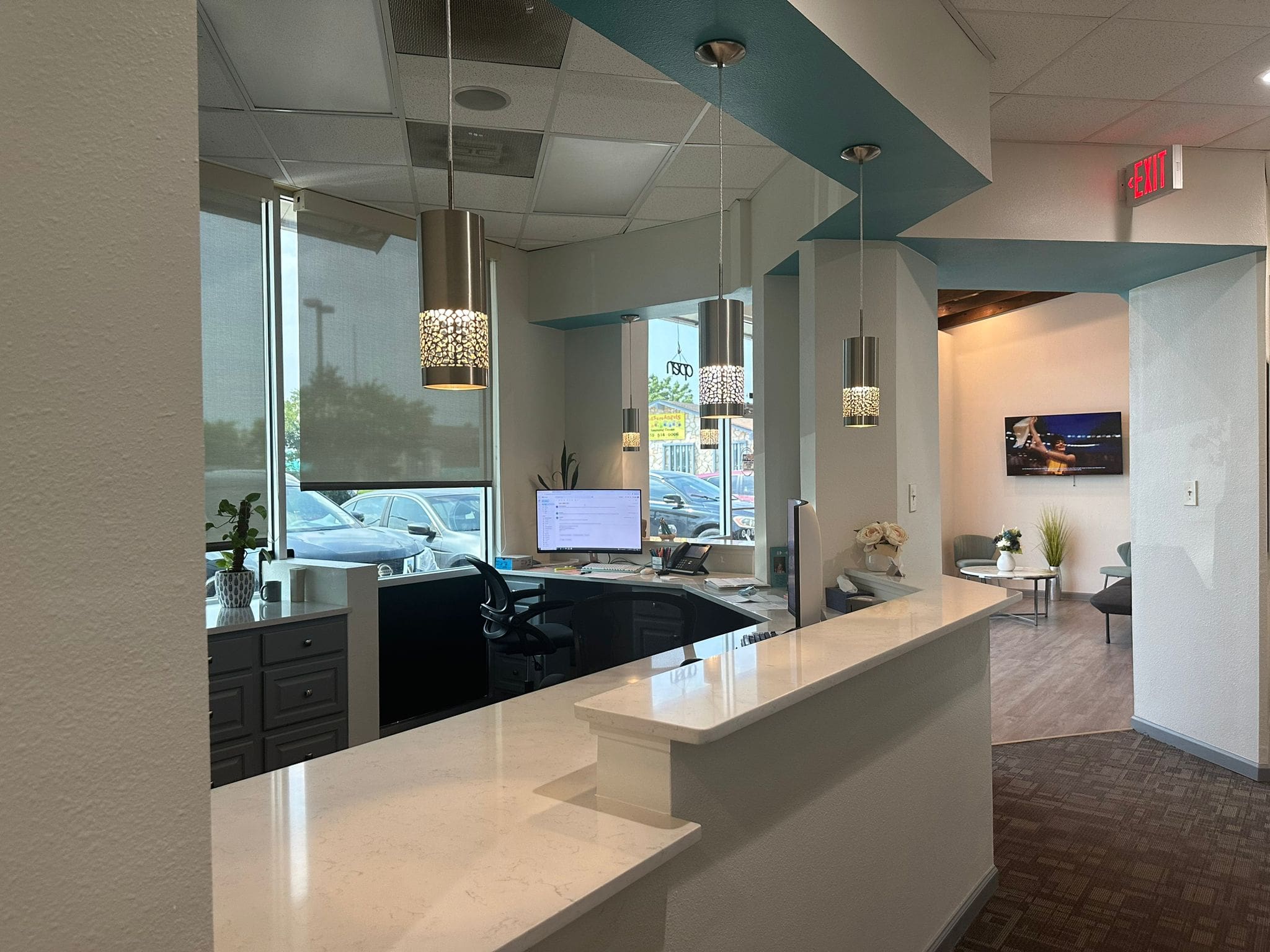 Welcome to Fiesta Orthodontics, where our dental office reception area features a sleek curved white counter, modern computer, and decorative hanging lights. Enjoy window views of cars outside as you await your free orthodontic consultation in comfort and style in San Antonio, TX