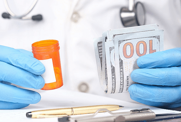 A person wearing blue gloves holds a pill bottle in one hand and a stack of hundred-dollar bills in the other, hinting at an Invisalign payment plan. A pen and stethoscope lie nearby on the table, completing the scene in San Antonio, TX