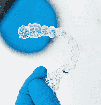 A gloved hand delicately holds a clear dental aligner, symbolizing the path to a perfect smile with an Invisalign payment plan, set against a calming blue background in San Antonio, TX