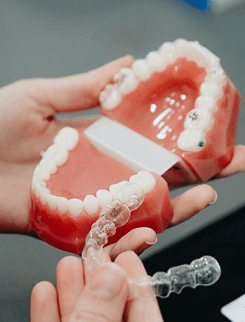 Hands holding a dental model and a clear aligner, illustrating how the aligner fits onto the teeth—a seamless solution available with an Invisalign payment plan in San Antonio, TX