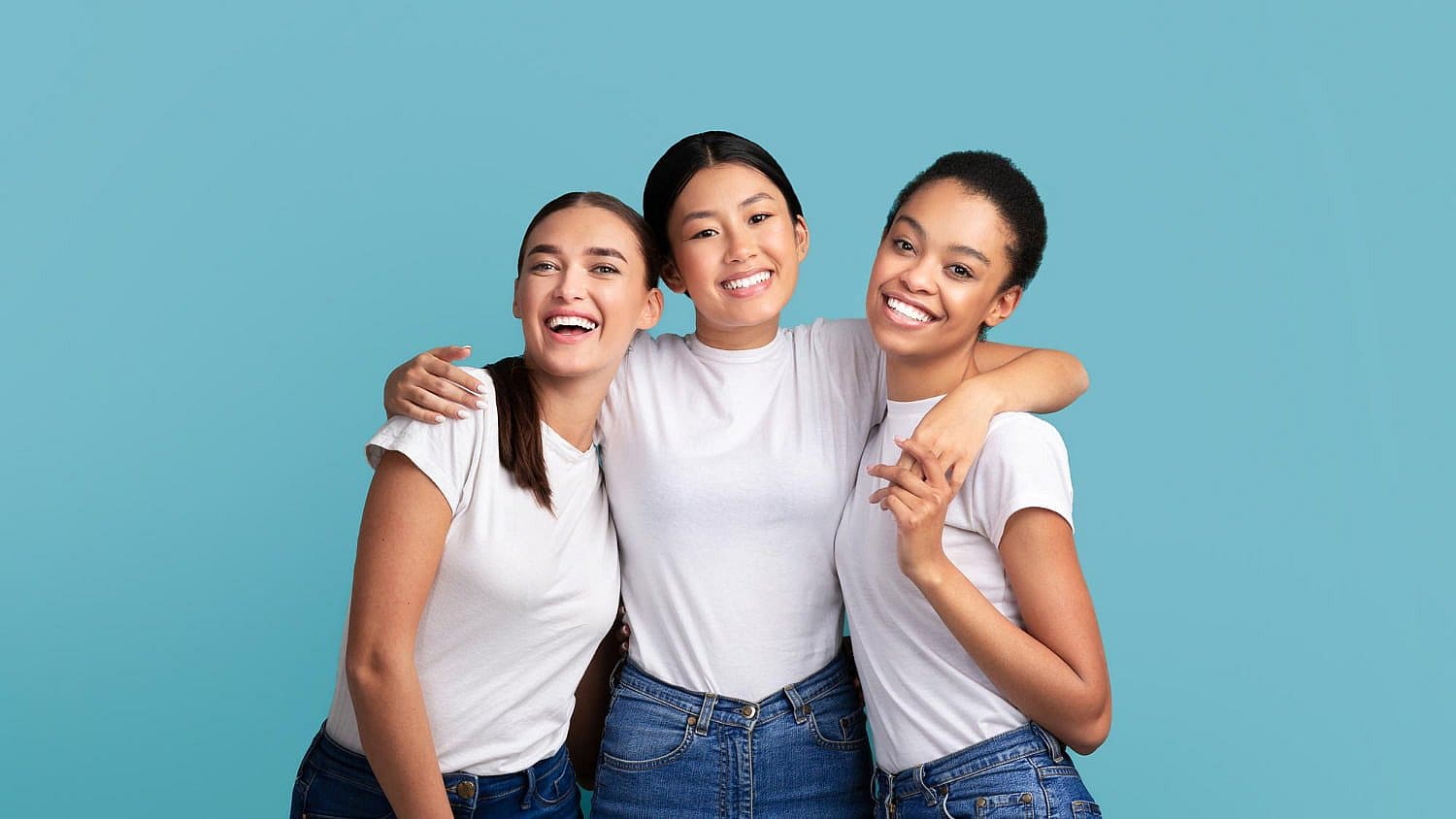 Three people in white shirts and blue jeans smile and pose against a plain blue background, embodying the vibrant spirit of Fiesta Orthodontics, one orthodontic expert in San Antonio, TX