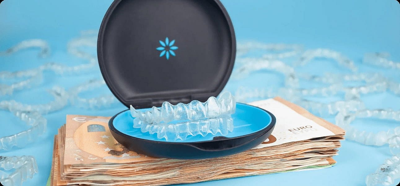 An Invisalign cost illustration in an open case rests atop a stack of euro banknotes, with more retainers scattered in the background on a blue surface in San Antonio, TX