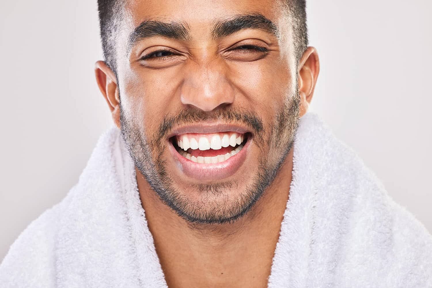 Smiling man with stubble, casually exuding a laid-back charm in his white bathrobe, against a plain background—his relaxed demeanor almost reminiscent of a carefree mouth breather in San Antonio, TX