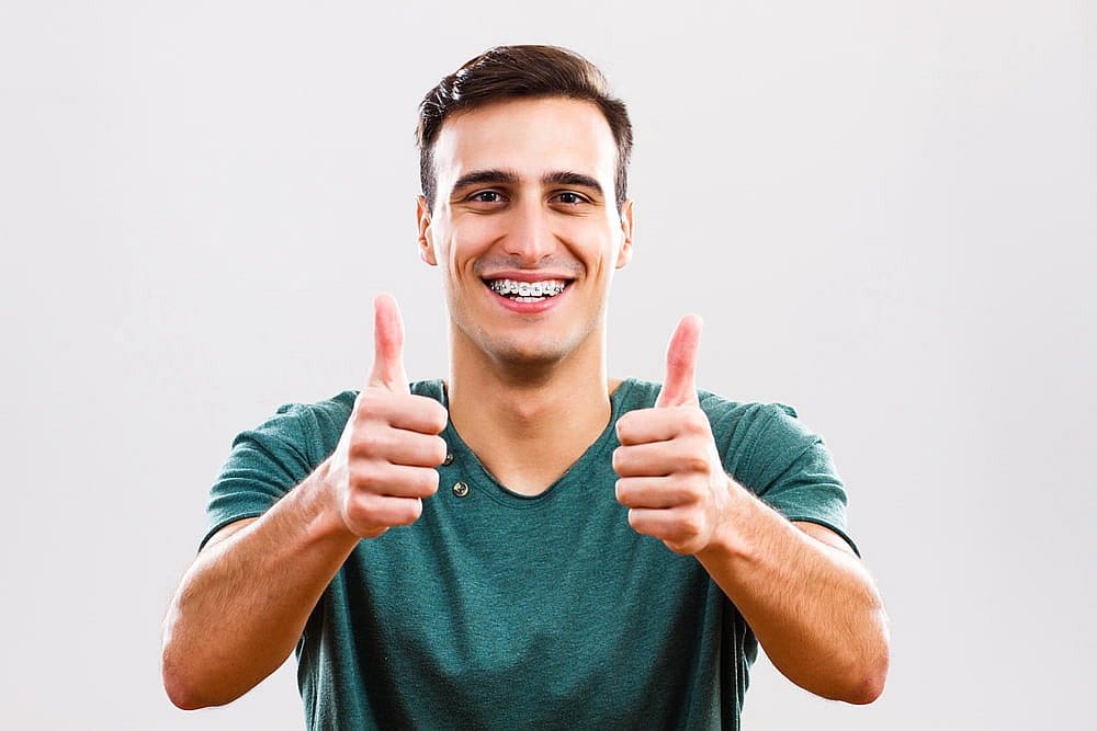 Man in a green shirt, flashing metal braces and smiling broadly while giving two thumbs up in San Antonio, TX