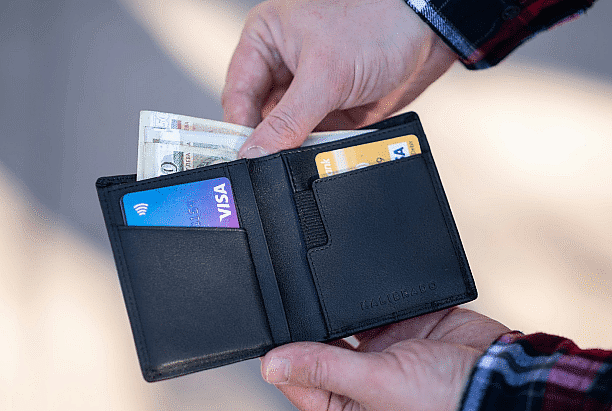 A person holds an open black wallet with cash and two credit cards, including a Visa card, perhaps considering how these funds will fit into their Invisalign payment plan in San Antonio, TX