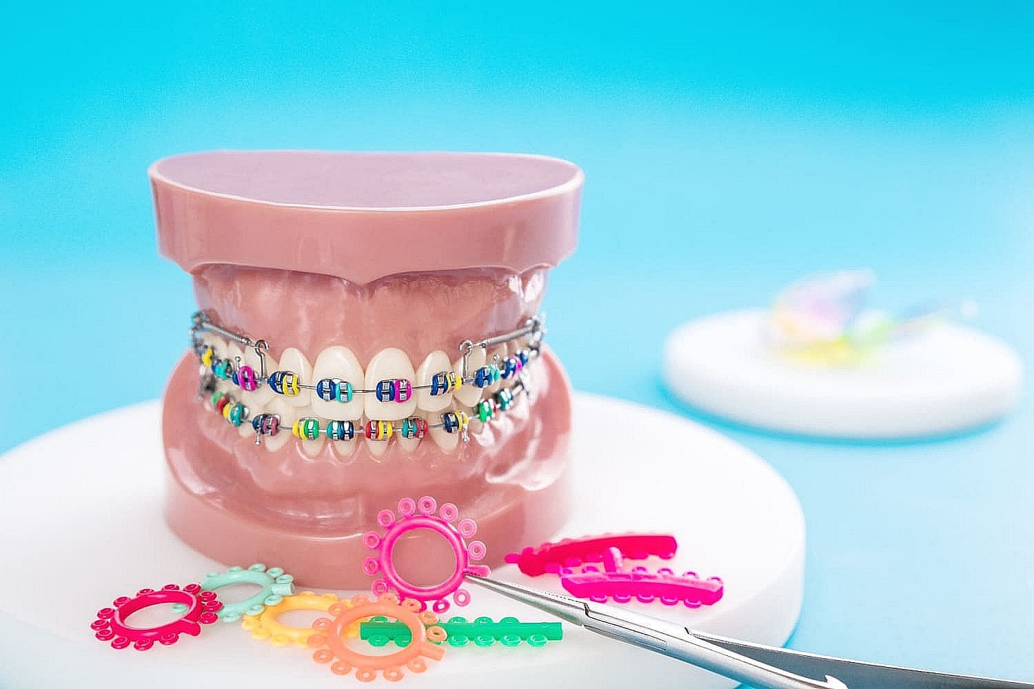 A dental model with metal braces showcases colorful elastic bands. Various colored bands and dental tools are artfully displayed in the foreground in San Antonio, TX