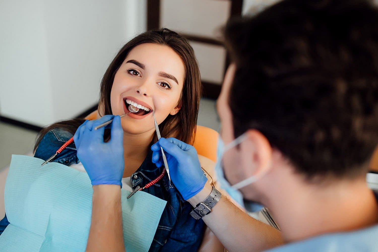 A woman at a dental appointment sits in a chair, smiling, as the dentist in gloves examines her teeth with instruments, paying particular attention to her underbite in San Antonio, TX