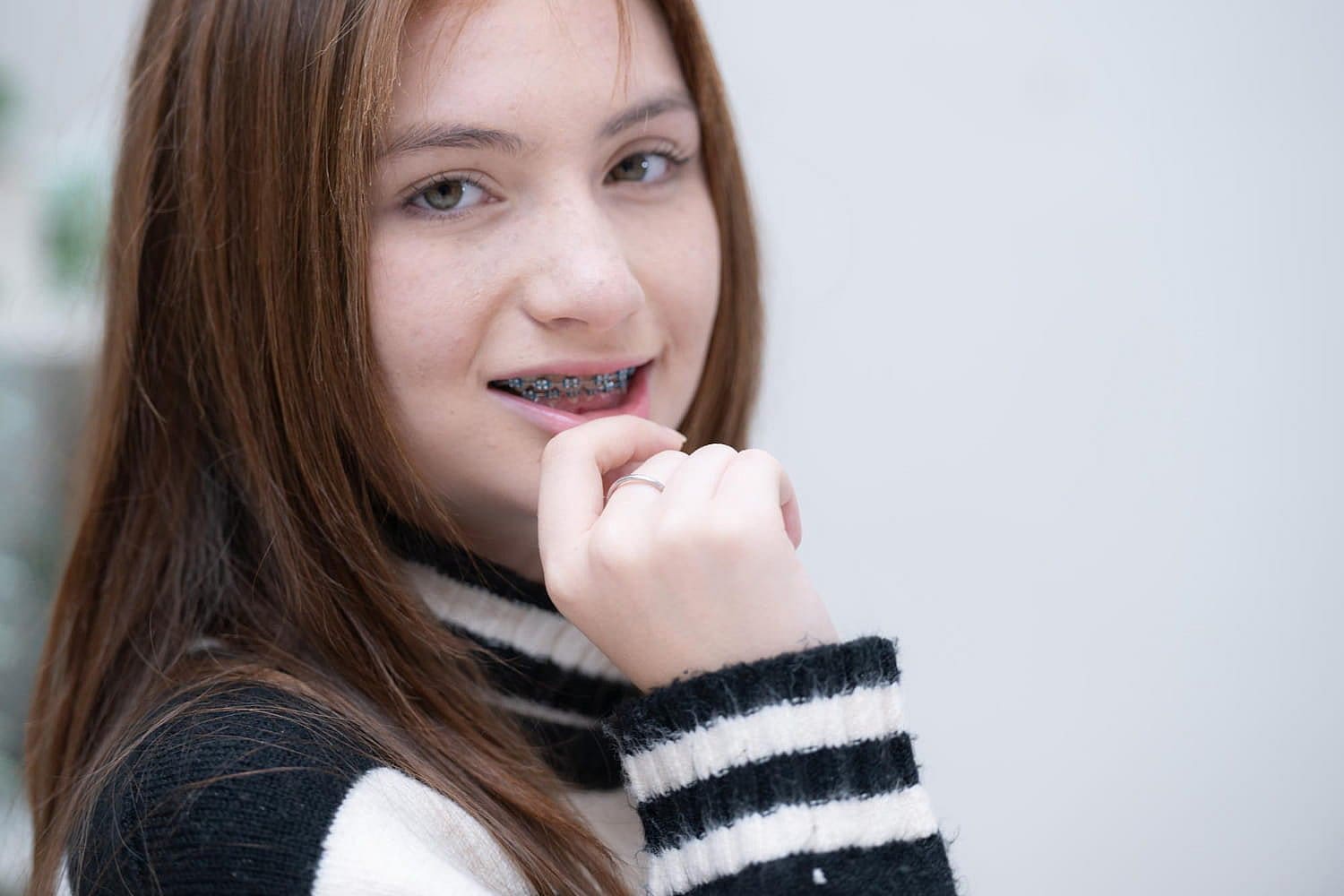 A young person with long hair and metal braces beams near me, sporting a black and white striped sweater in San Antonio, TX