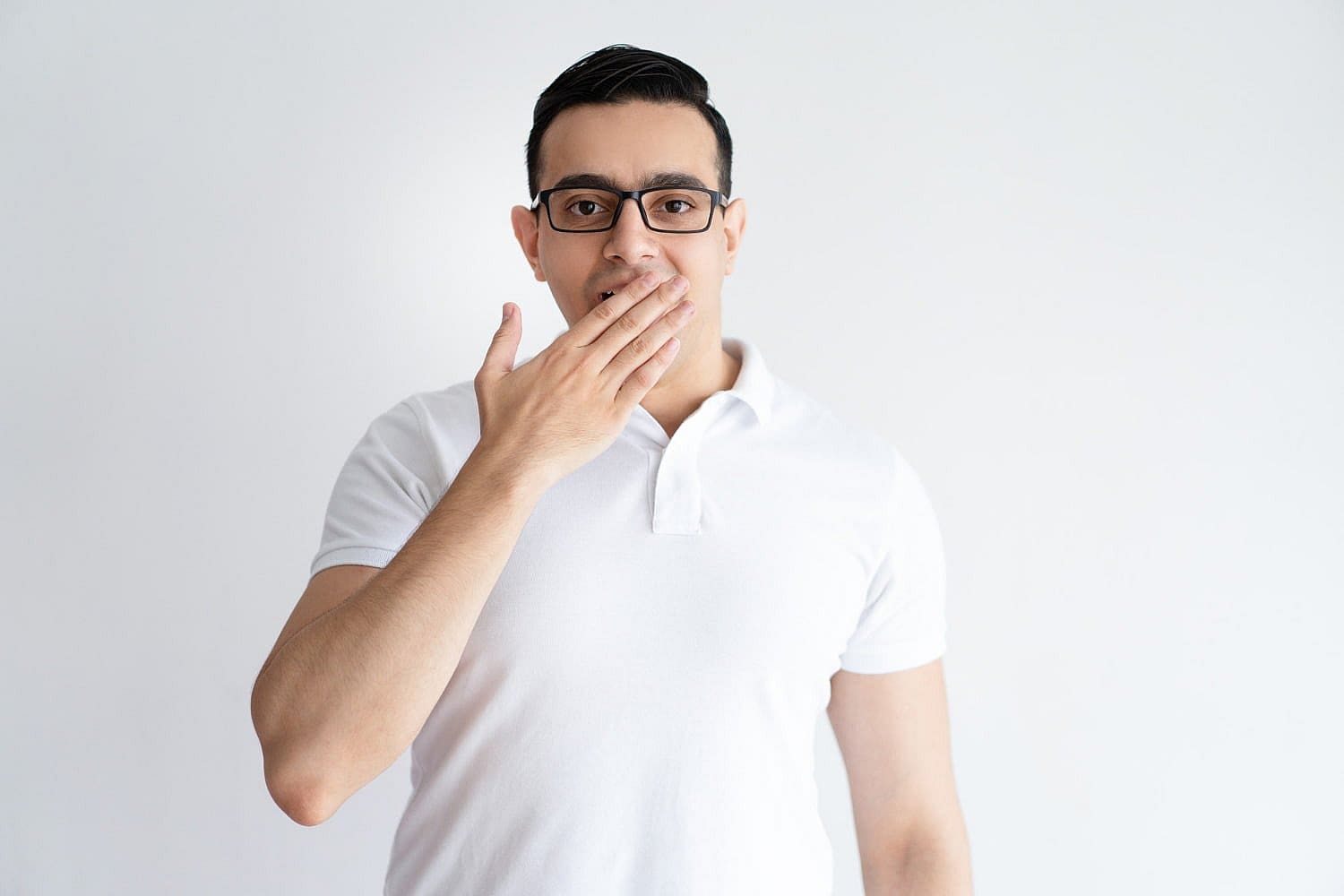 A man in a white polo shirt and glasses discreetly covers his mouth with his hand, perhaps warding off being labeled a "mouth breather," standing against a plain white background in San Antonio, TX