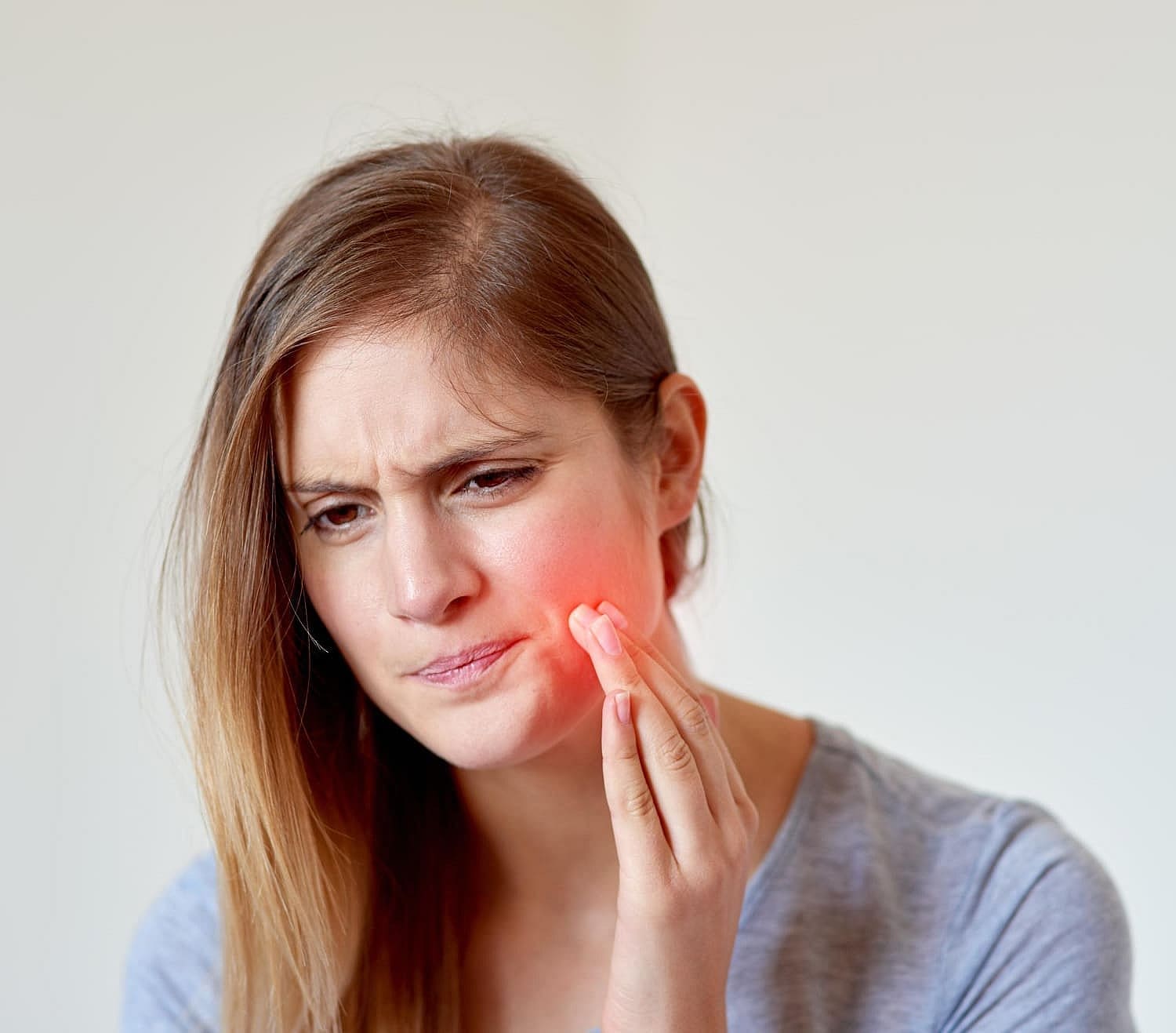 A woman with long hair touches her cheek, indicating discomfort often seen in discussions of Invisalign vs Braces. Her face shows a pained expression, with a red area highlighting the affected spot in San Antonio, TX