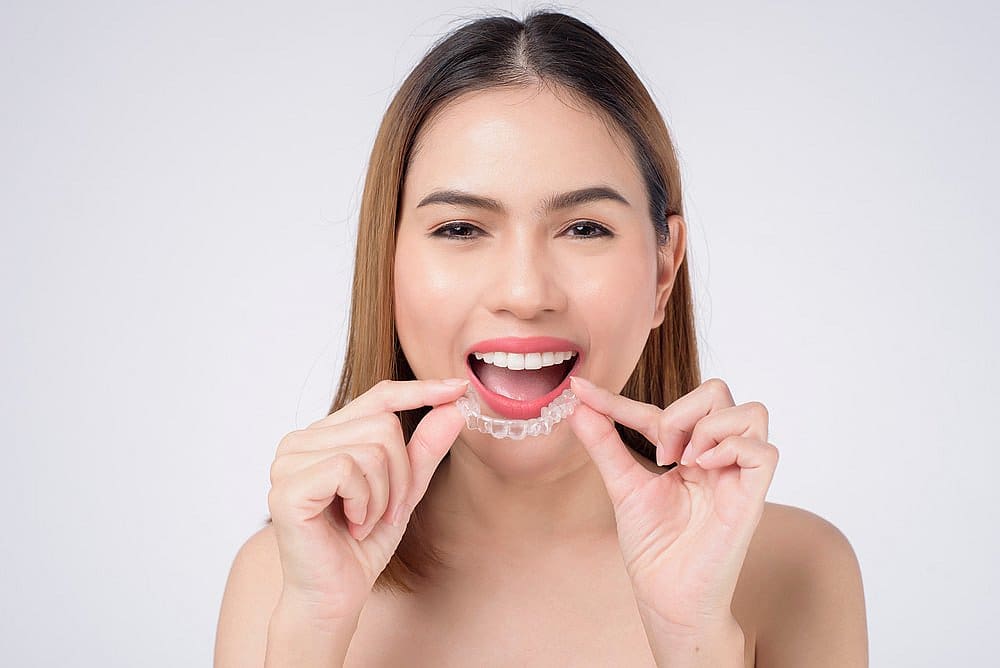 A person carefully inserts their clear dental aligners into their mouth against a plain background, considering an Invisalign payment plan to achieve their dream smile in San Antonio, TX