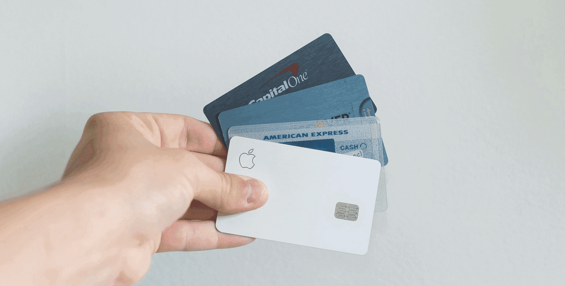 A hand displays a fan of five credit cards, including Capital One, American Express, and an Apple Card—essential tools for managing expenses or even flexible options like an Invisalign payment plan—set against a plain white background in San Antonio, TX