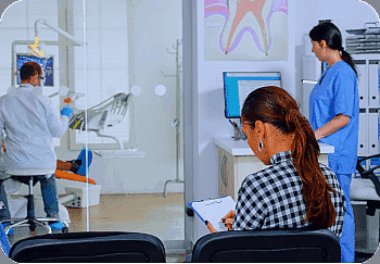 A woman in a checkered shirt sits in a waiting area with a clipboard, reviewing orthodontic insurance plans. Meanwhile, a dentist and assistant attentively work on a patient in the background in San Antonio, TX