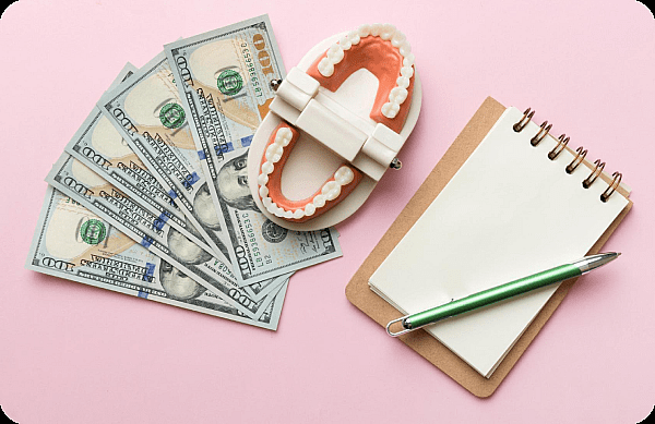 A dental model and metal braces rest beside several $100 bills, a notepad, and a green pen on a pink surface in San Antonio, TX