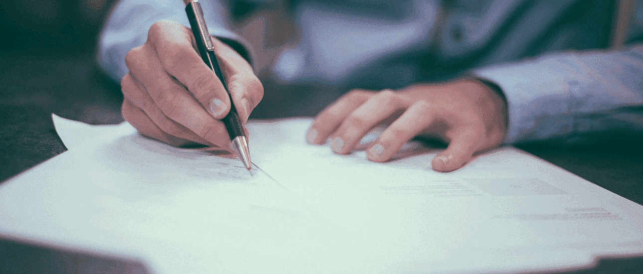 A person in a blue shirt is deeply focused, writing with a pen on paper, meticulously organizing handwritten notes and documents related to orthodontic insurance plans scattered across the desk in San Antonio, TX