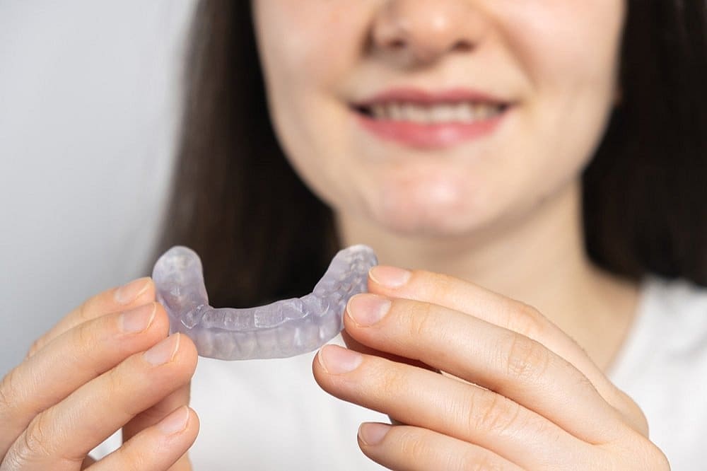 A person holding a transparent dental aligner in front of their mouth, revealing a partial smile, reminiscent of the comfort offered by a TMJ mouth guard in San Antonio, TX