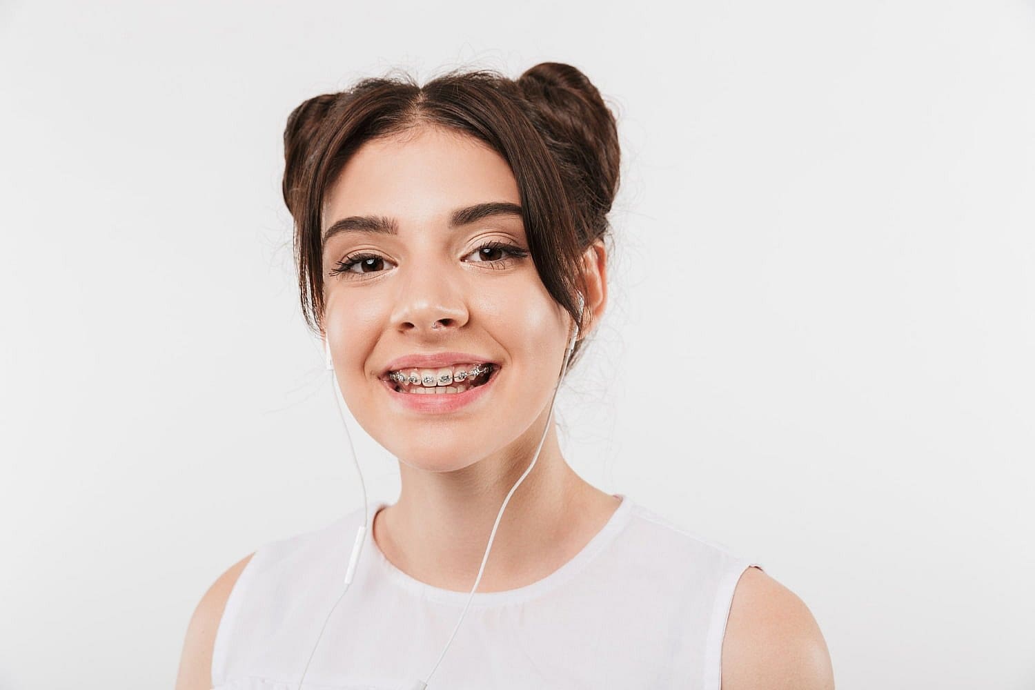 Young woman with affordable braces and earbuds smiles at the camera against a plain white background in San Antonio, TX