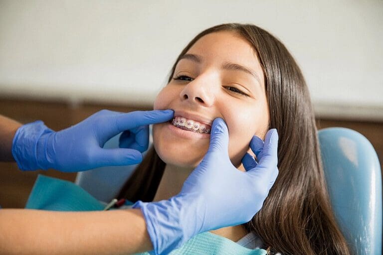 At Fiesta Orthodontics, a dentist wearing blue gloves examines a smiling girl's braces, demonstrating quality braces for overbite in San Antonio, TX.