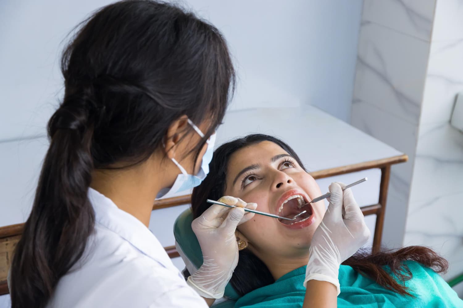 A dentist at Fiesta Orthodontics in East San Antonio, TX, checks a female patient's teeth with orthodontic appliances.