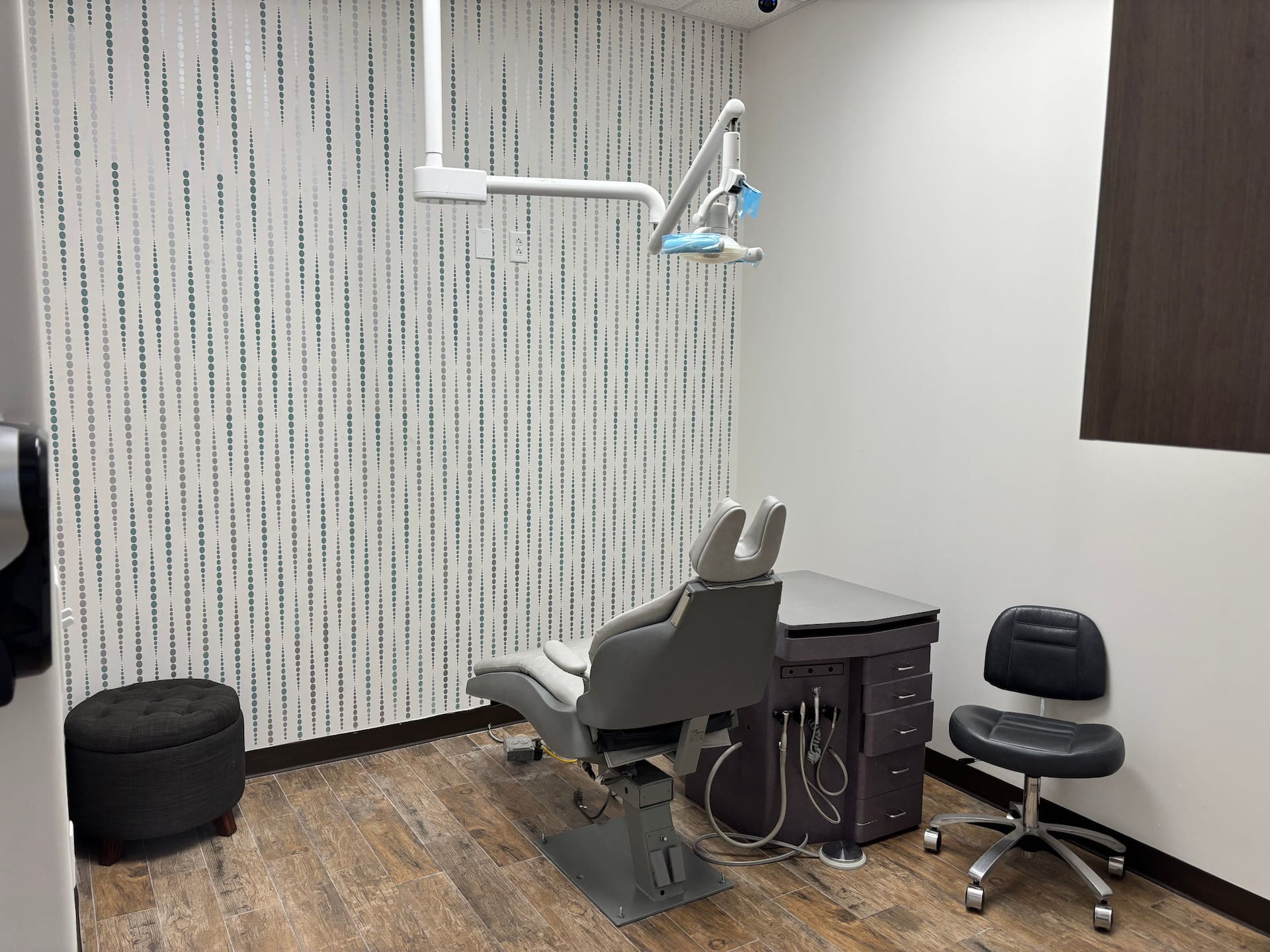 A modern dental exam room at Fiesta Orthodontics in East San Antonio, TX, featuring a chair, equipment station, stool, and patterned wall.