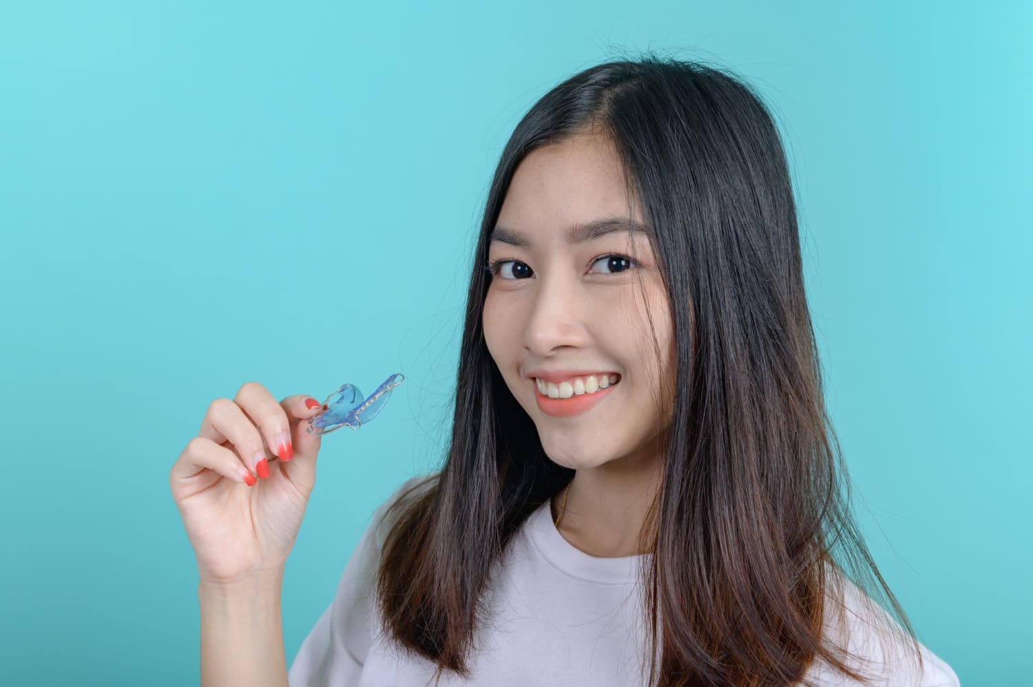 Smiling young woman with long dark hair holds a clear dental retainer, representing orthodontic appliances at Fiesta Orthodontics in East San Antonio, TX.