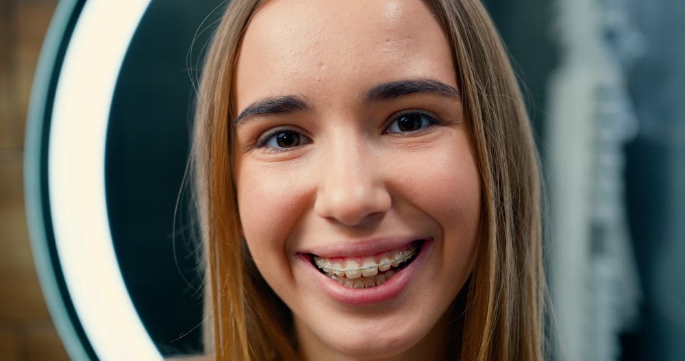 Smiling teen with straight brown hair and clear ceramic braces at Fiesta Orthodontics in East San Antonio, TX.