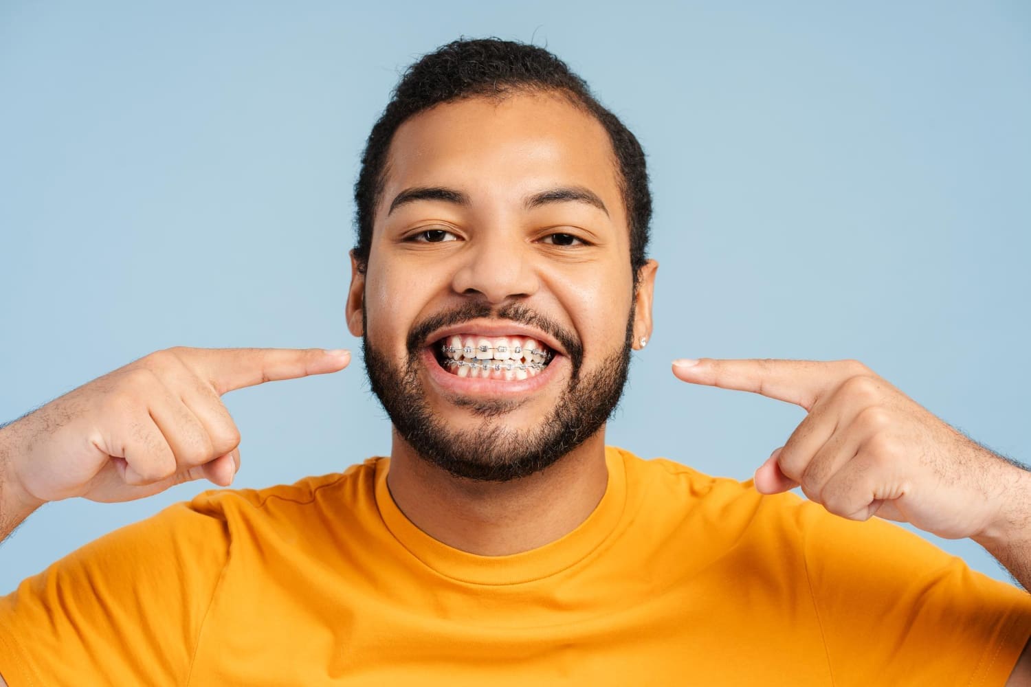 Smiling man in an orange shirt points at new braces, promoting Fiesta Orthodontics in West San Antonio and East San Antonio, TX.