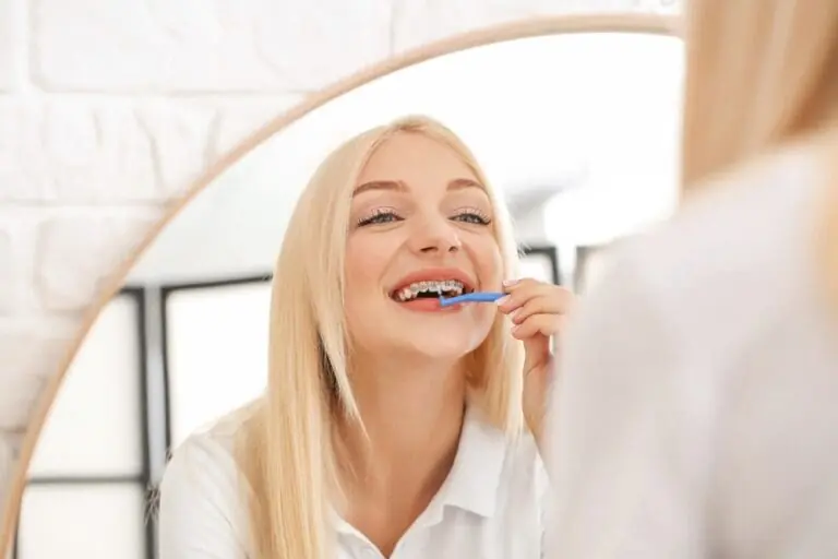 young woman metal braces toothbrush home - How to Floss with Braces in San Antonio, TX.