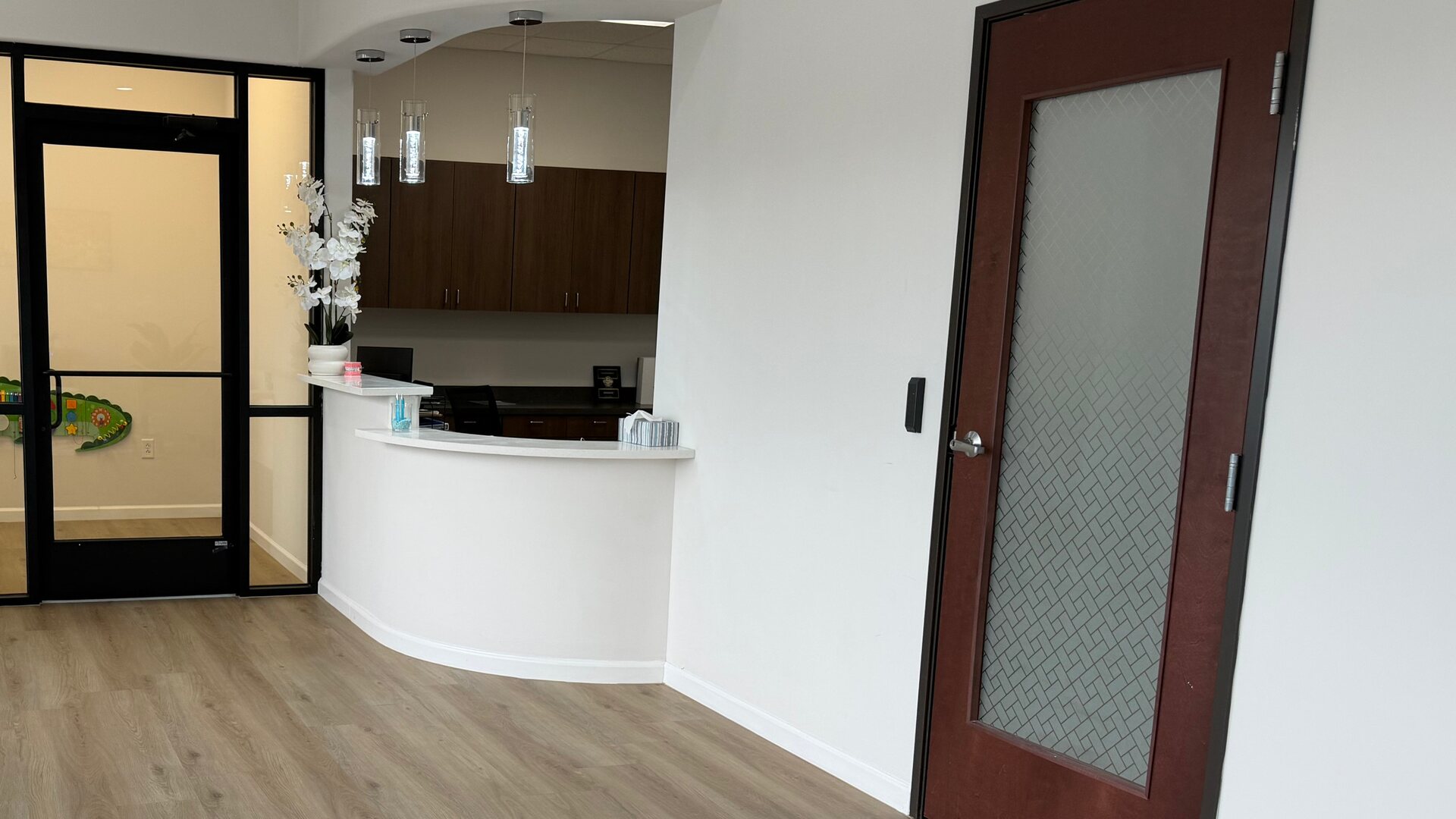 Curved front desk with pendant lights, the glass door of the kids room and a wood office door at Fiesta Orthodontics in East San Antonio, TX.